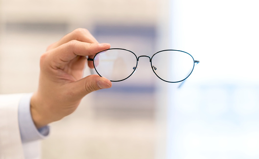 Close-up on an optician holding glasses at the optical shop â healthcare and medicine