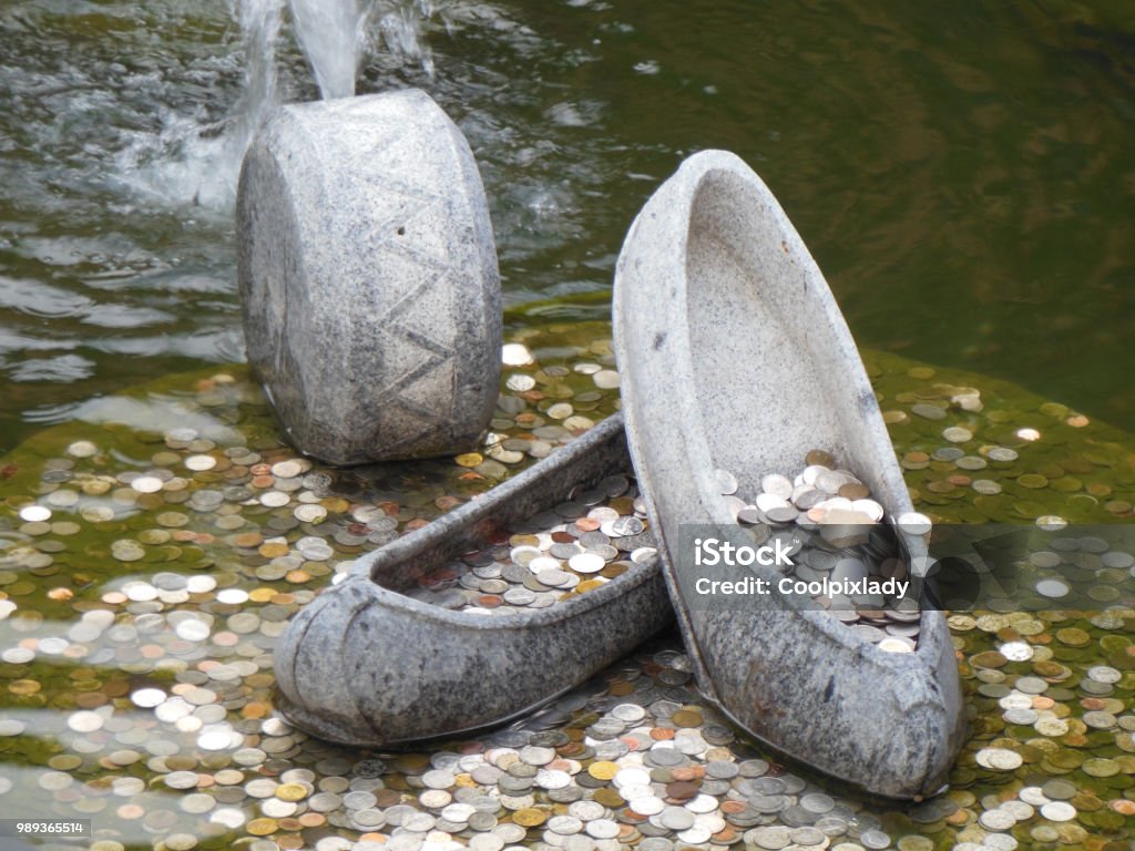 Coins in fountain with stone shoes Coins in fountain pond with stone shoes filled with money as symbol of good luck and fortune Fountain Stock Photo