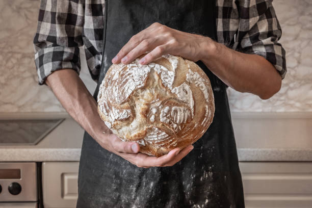 istock Person in black apron in home kitchen background with wheat bread 989376290
