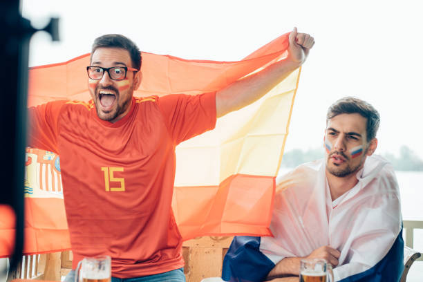 istock Excited Spanish soccer supporter shouting while watching the game with a friend 989381480