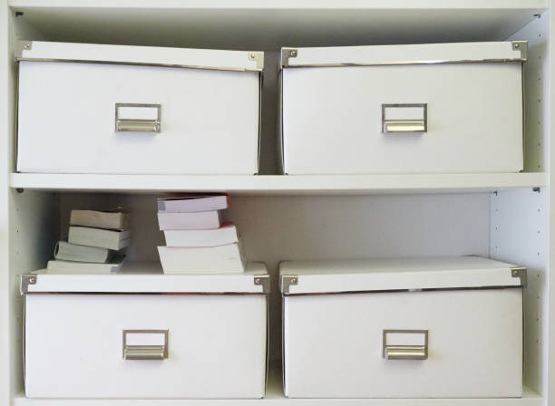istock Group of white boxes with naming plate on a shelve and some books 989395612