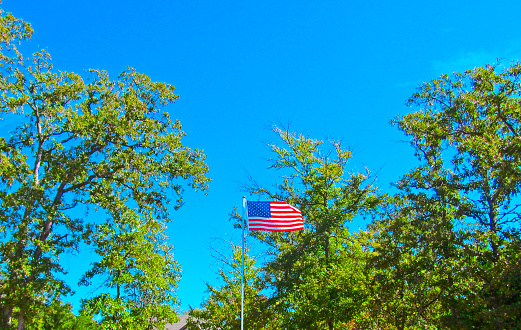 A bright sunny summer view of the flagpole with American flag in the wind.