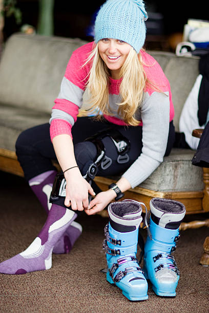 Portrait of  woman skier adjusting knee brace. Smiling woman adjusts knee brace with ski boots in foreground. knee brace stock pictures, royalty-free photos & images