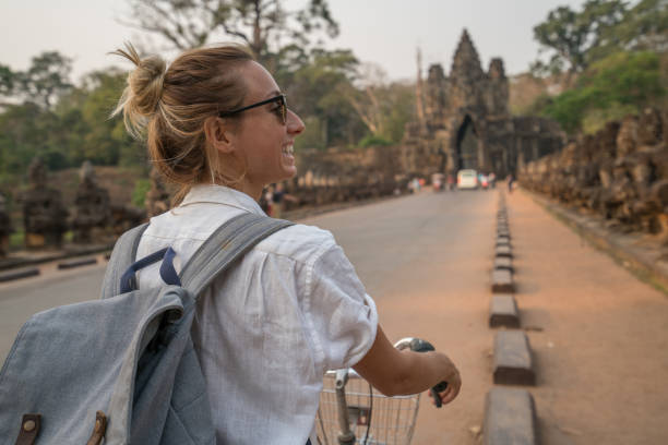 istock Young woman on bicycle in ancient temple complex in Cambodia 989505628