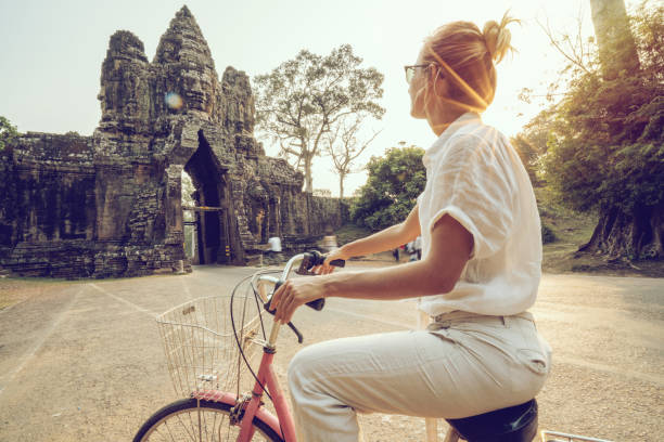 istock Young woman on bicycle in ancient temple complex in Cambodia 989507640