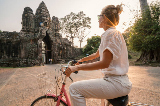 istock Young woman on bicycle in ancient temple complex in Cambodia 989510408