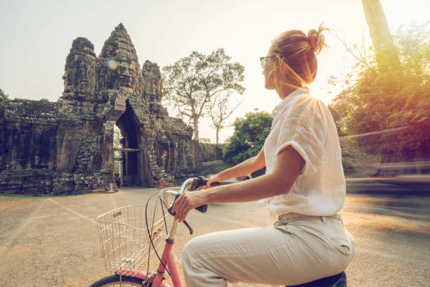 istock Young woman on bicycle in ancient temple complex in Cambodia 989510790