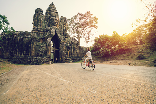 Young woman traveling in Cambodia visiting the temples of Angkor wat complex by bicycle. People travel discovery Asia concept. Shot at sunset, one woman only, adventure and exploration in Siem Reap, Southeast Asia.