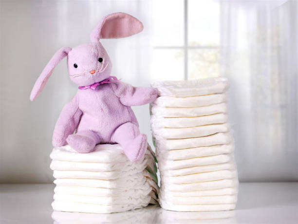Stack of baby diapers on table with funny bunny. Bright background. Stack of baby diapers on table with funny bunny. Bright background. baby goods stock pictures, royalty-free photos & images