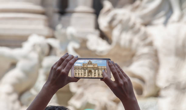 Women hand take pictures with a mobile phone of Italian Famous Place Trevi Fountain in Rome summer sunny day stock photo