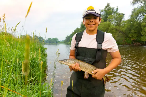 Photo of Young fisherman holding a pike he has just caught.