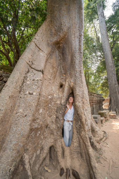 istock Girl in ancient temple complex hiding in enormous tree, big roots 989570492