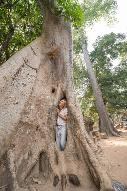 istock Girl in ancient temple complex hiding in enormous tree, big roots 989573362