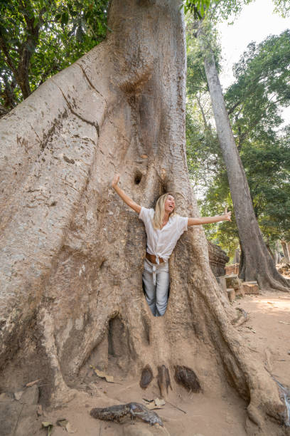 istock Girl in ancient temple complex hiding in enormous tree, big roots 989576010