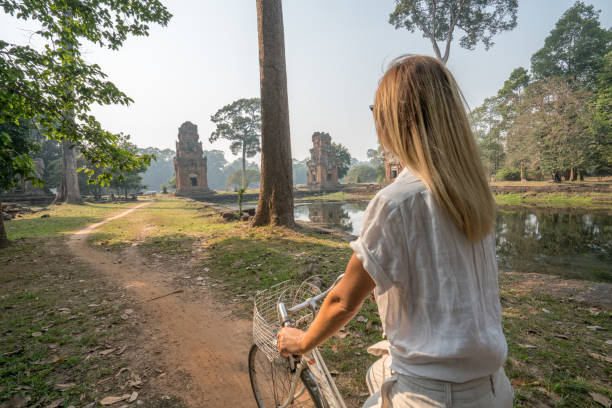 istock Young woman on bicycle in ancient temple complex in Cambodia 989580252