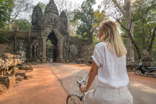 istock Young woman on bicycle in ancient temple complex in Cambodia 989598228
