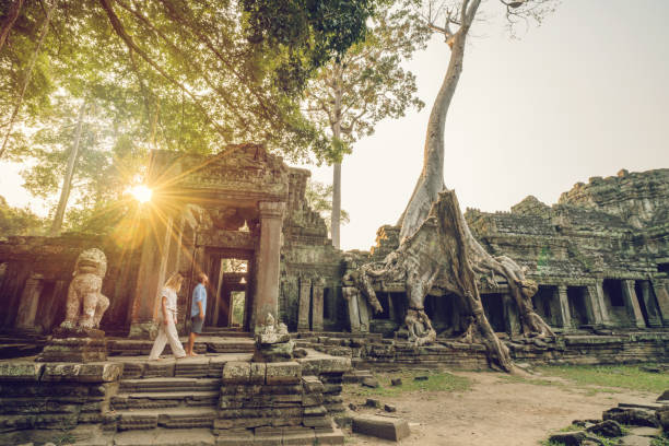 wonderlust- coppia che vaga nell'antico tempio con radici che prendono il controllo di vecchie rovine- complesso cambogiano angkor wat al tramonto - angkor wat buddhism cambodia tourism foto e immagini stock