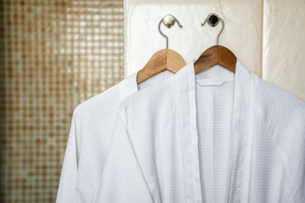 badjassen-handdoeken van de twee witte doek op houten hangers in het interieur van een stijlvolle badkamer. ontspannen in het hotel voor twee. - badjas stockfoto's en -beelden