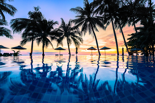 Summer beach holiday vacation destination, luxurious beachfront resort swimming pool with tropical landscape, quiet warm sunset, silhouette and reflection in water