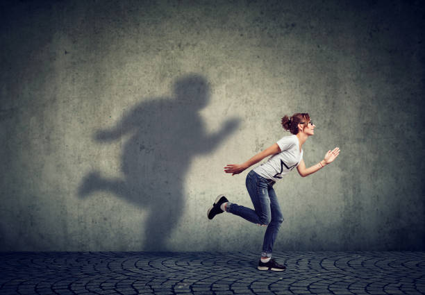 istock Woman running away from her fat shadow on the wall 989670236