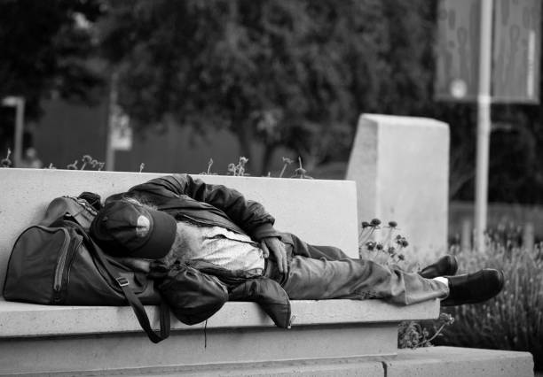 Los Angeles, USA- June 2018:  A man sleeping on a bench with his bag underneath his head, in a public park in Los Angeles downtown. Black and white photo.
