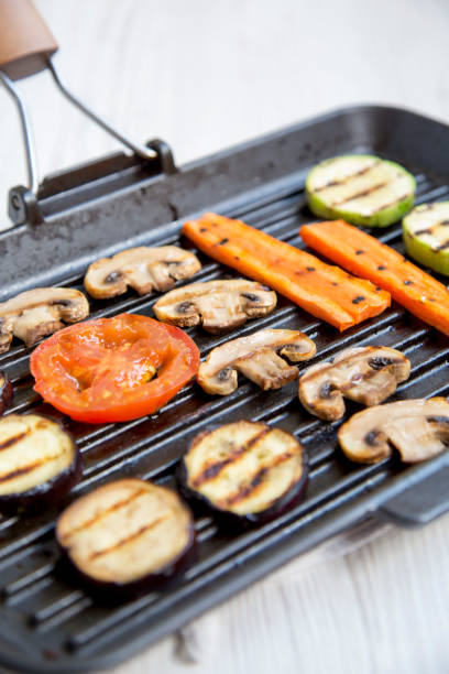 istock Grilled vegetables in a grilling pan on a white wooden background, side view. Close-up. 989713864