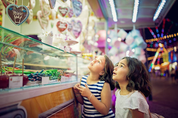 Two little girls are looking sweets in the candy wagon at the fun fair Two little girls are looking sweets in the candy wagon at the fun fair window shopping at night stock pictures, royalty-free photos & images