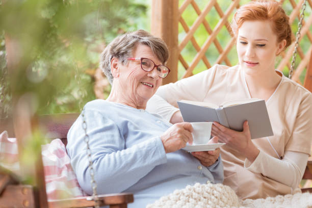 istock Happy elderly woman drinking tea while nurse reading book in the garden 989795592