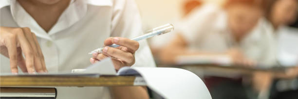 istock School student's taking educational exam, thinking hard, writing answer with left hand in classroom for education, university admission test  and world literacy day concept 989797884