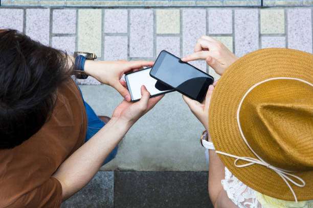 Young asian couple using smart phone outside. Young Japanese woman adding male friend to her LINE friends list by reading his QR Code. asian couple playing in phone stock pictures, royalty-free photos & images