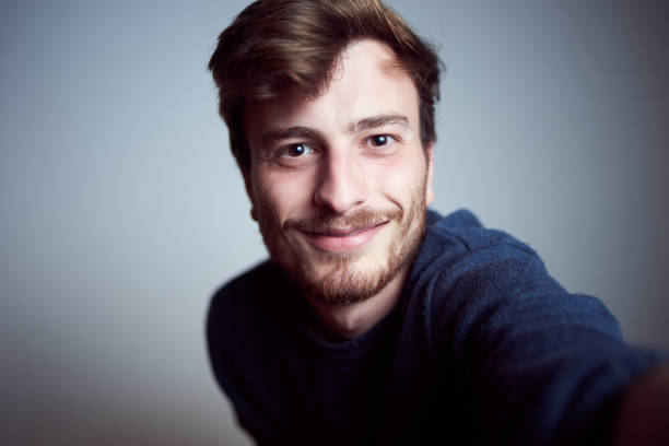 Cute young male looking at camera and smiling in the studio. Real people taking a self portrait alone with a happy face stock photo