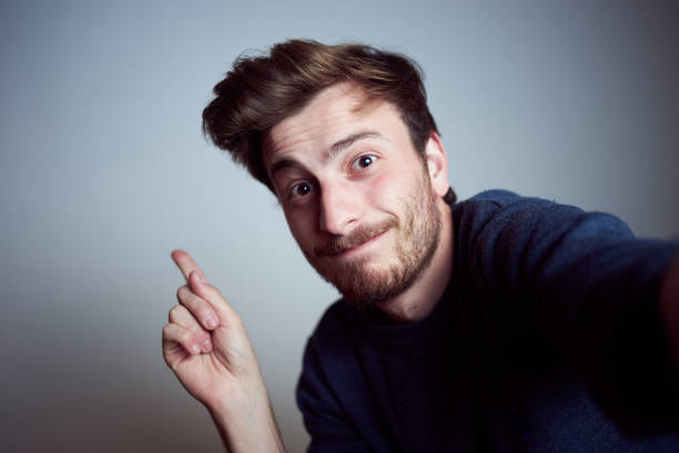 Young happy teenager male looking at camera and pointing up with his finger alone in the studio stock photo