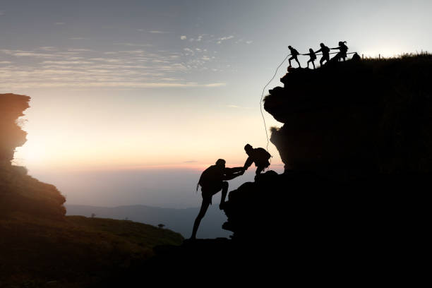 hike climbing mountain . Male and female hikers climbing up silhouette mountain cliff . teamwork ,success ,helps , business concept. team effort stock pictures, royalty-free photos & images