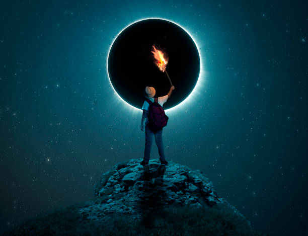 istock Traveler kid holding a torch on a peak in front of  eclipse. 989956650