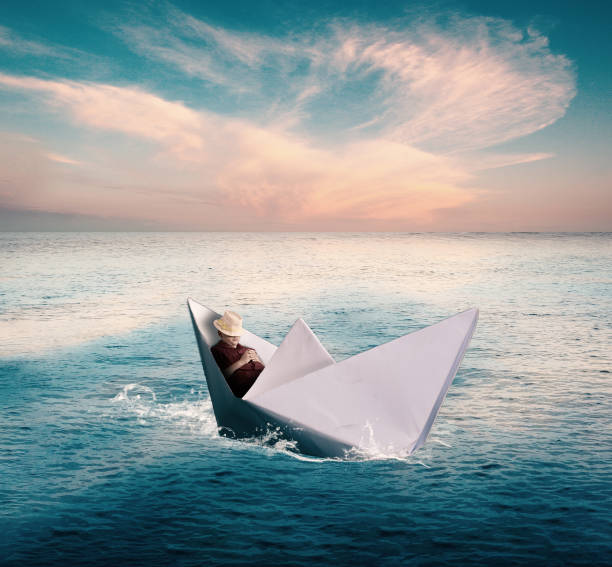 istock Young man taking a nap in a paper boat while sailing on the sea. 989956698
