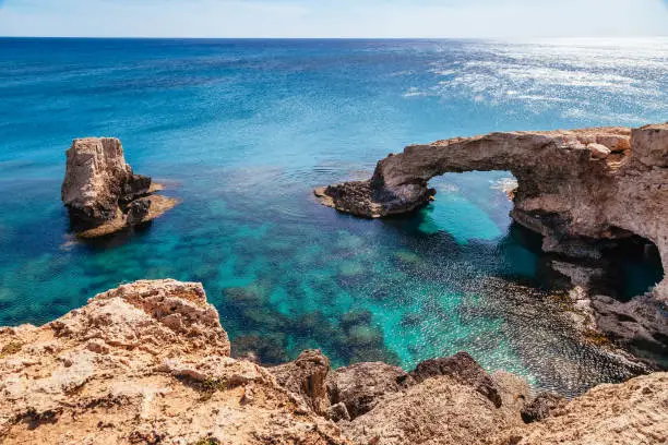 Photo of Beautiful natural rock arch near of Ayia Napa, Cavo Greco and Protaras on Cyprus island, Mediterranean Sea. Legendary bridge lovers. Amazing blue green sea and sunny day.
