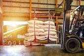 Forklift handling white sugar bags for stuffing into containers outside a warehouse.