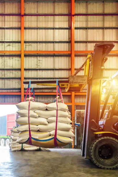 Photo of Forklift handling white sugar bags for stuffing into containers outside a warehouse.