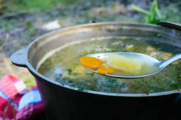 Photo of Fish soup boils in cauldron at the stake on the nature. Soup in a pot in the fire. Close-up.