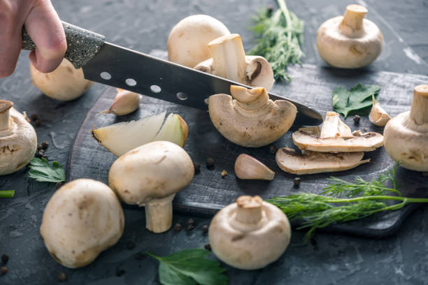 istock Women's hands are cutting champignons with a knife on the dark kitchen table. Cooking mushroom dishes. Close up 990104792
