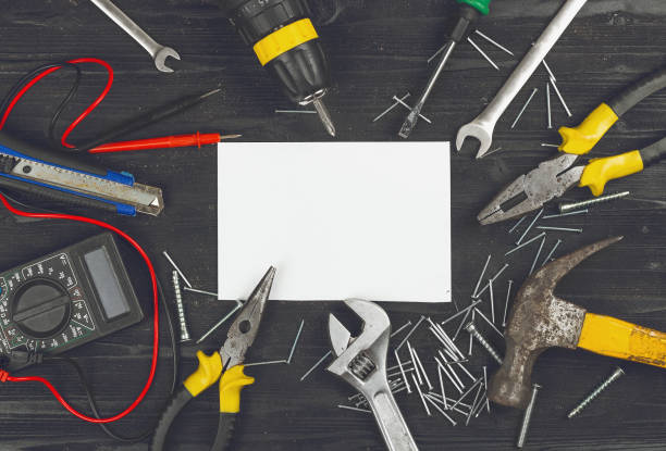 istock Top view on set of working hand tools,wrench, screwdriver, pliers, hammer, adjustable spanner, office knife, scattered nails and screws, digital multimeter, blank sheet of paper on black wooden table. 990118710