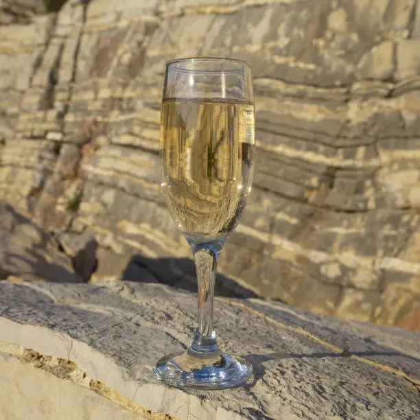 A glass of wine against the background of a rock at sunset.