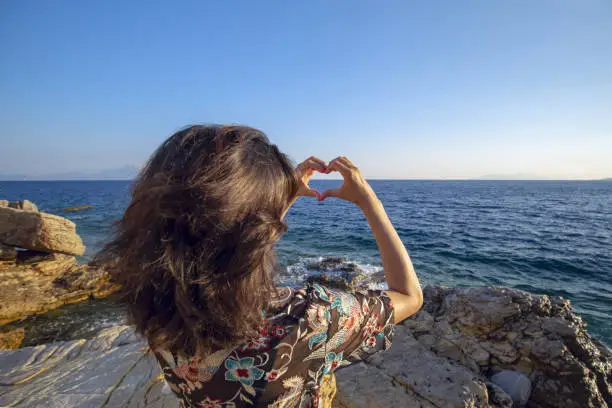 A girl makes hearts with her hands and looks at the sunset in the sea. Sign - I love the sea.