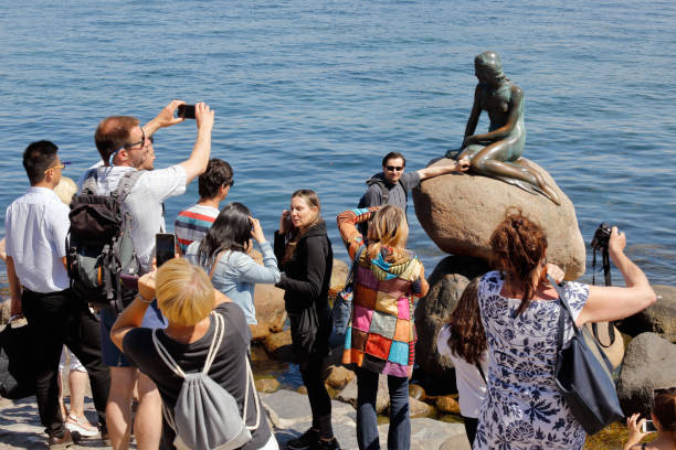 Copenhagen, Denmark - June 27, 2018: Tourists infront of the bronze statue of the Little Mermaid, by Edvard Eriksen, located at Langelinie.