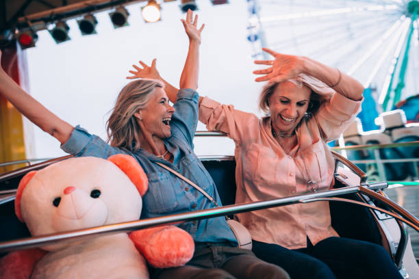 Excited mature women riding roller coaster with arms outstretched