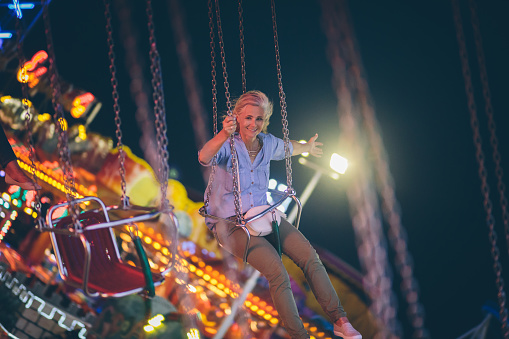 Excited mature woman on summer vacations enjoying amusement park chairoplane ride with arms outstretched