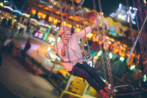 Smiling senior woman on summer holidays having fun riding fairground chairoplane ride at night