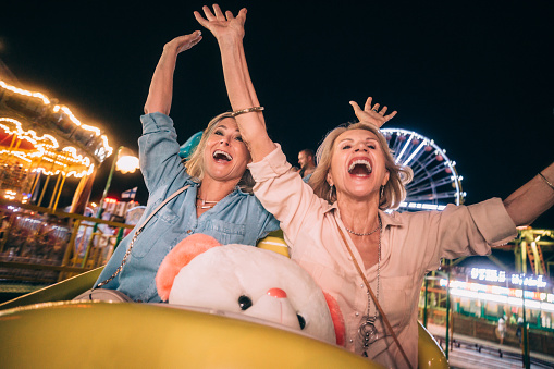 Excited senior friends enjoying amusement park roller coaster ride together