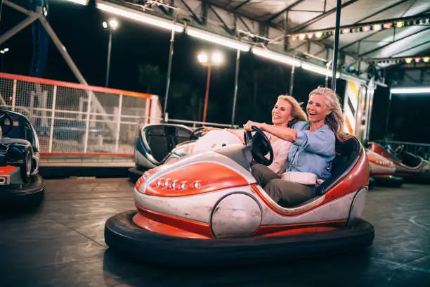 Excited mature women on summer holidays having fun driving dodgem cars at travelling carnival