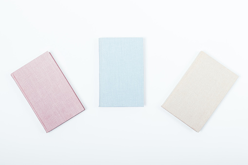 Minimal flat lay composition of three books: pink, blue and beige on a white background. Notebooks with blank covers, top view.